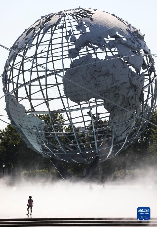 2021年8月13日，一名儿童冒着高温天气站在美国纽约科罗纳公园水雾广场的地球模型前。新华社记者 王迎 摄